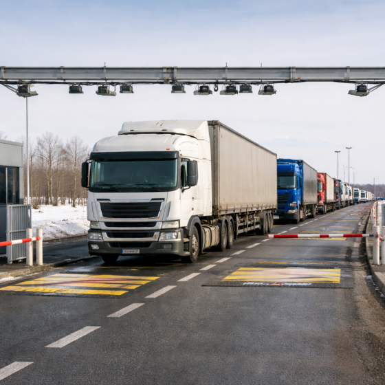 International truck border crossing lane in Ukraine with inspection gantry and queued freight trucks in winter daylight, no text